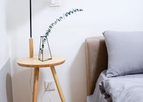 Modern minimalist bedroom with wooden nightstand, sleek lamp, and gray bedding set.